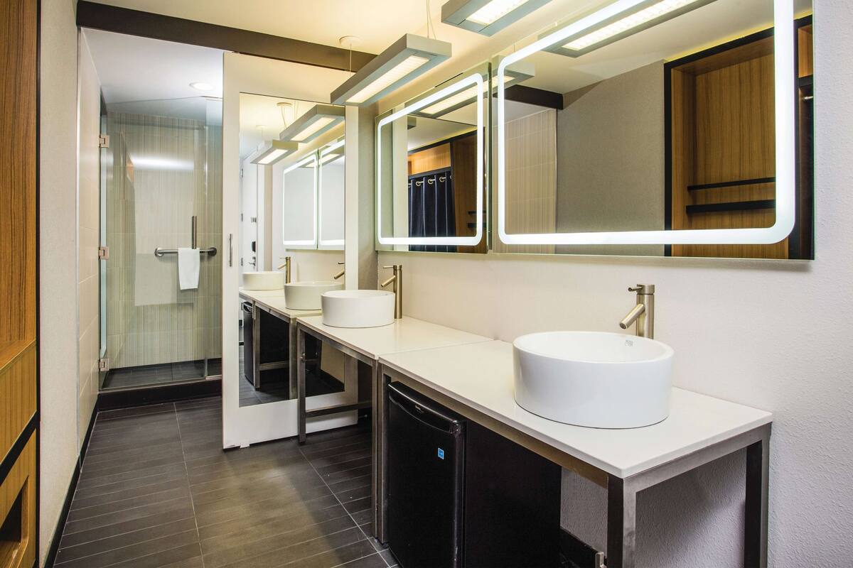 Une salle de bain moderne dotée d’une douche à parois de verre, d’un lavabo blanc avec un robinet doré et d’un miroir avec éclairage intégré.