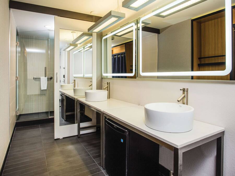 A modern bathroom with a glass shower enclosure, a white sink with a gold faucet, and a mirror with integrated lighting.