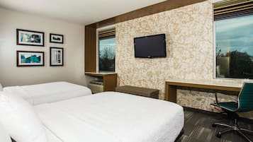 Une chambre d’hôtel avec deux lits, un bureau, une chaise, une télévision et des œuvres d’art accrochées au mur.