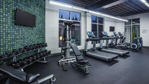 Une salle de sport équipée de tapis de course, de vélos elliptiques et d’haltères.