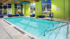 Une piscine intérieure à l’eau claire, avec des chaises longues bleues et un plafond en bois.