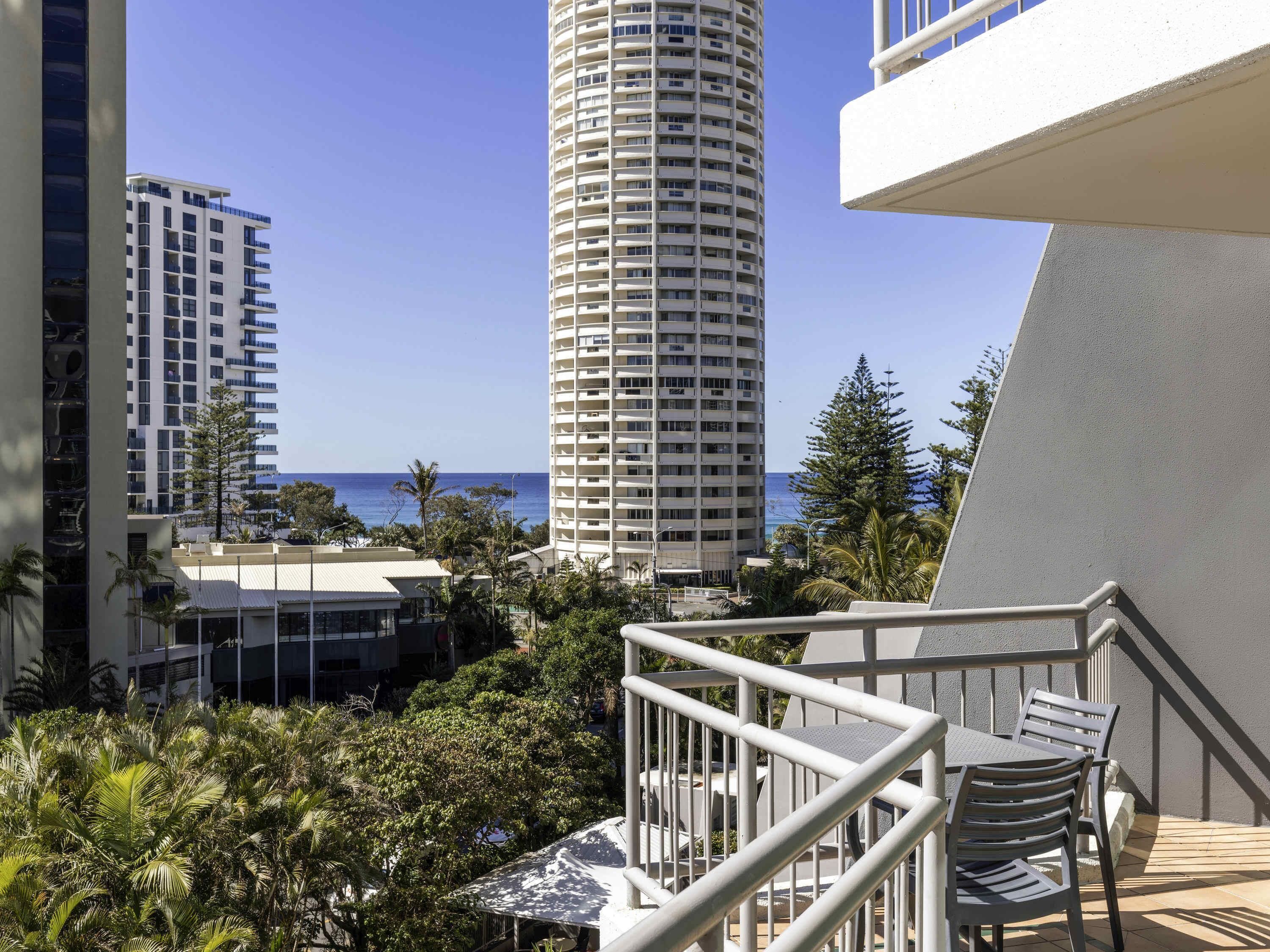 Un balcon agrémenté de mobilier d’extérieur, avec vue sur l’océan et de grands immeubles en arrière-plan.