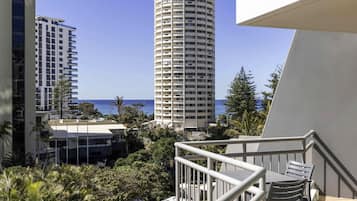 Un balcon agrémenté de mobilier d’extérieur, avec vue sur l’océan et de grands immeubles en arrière-plan.