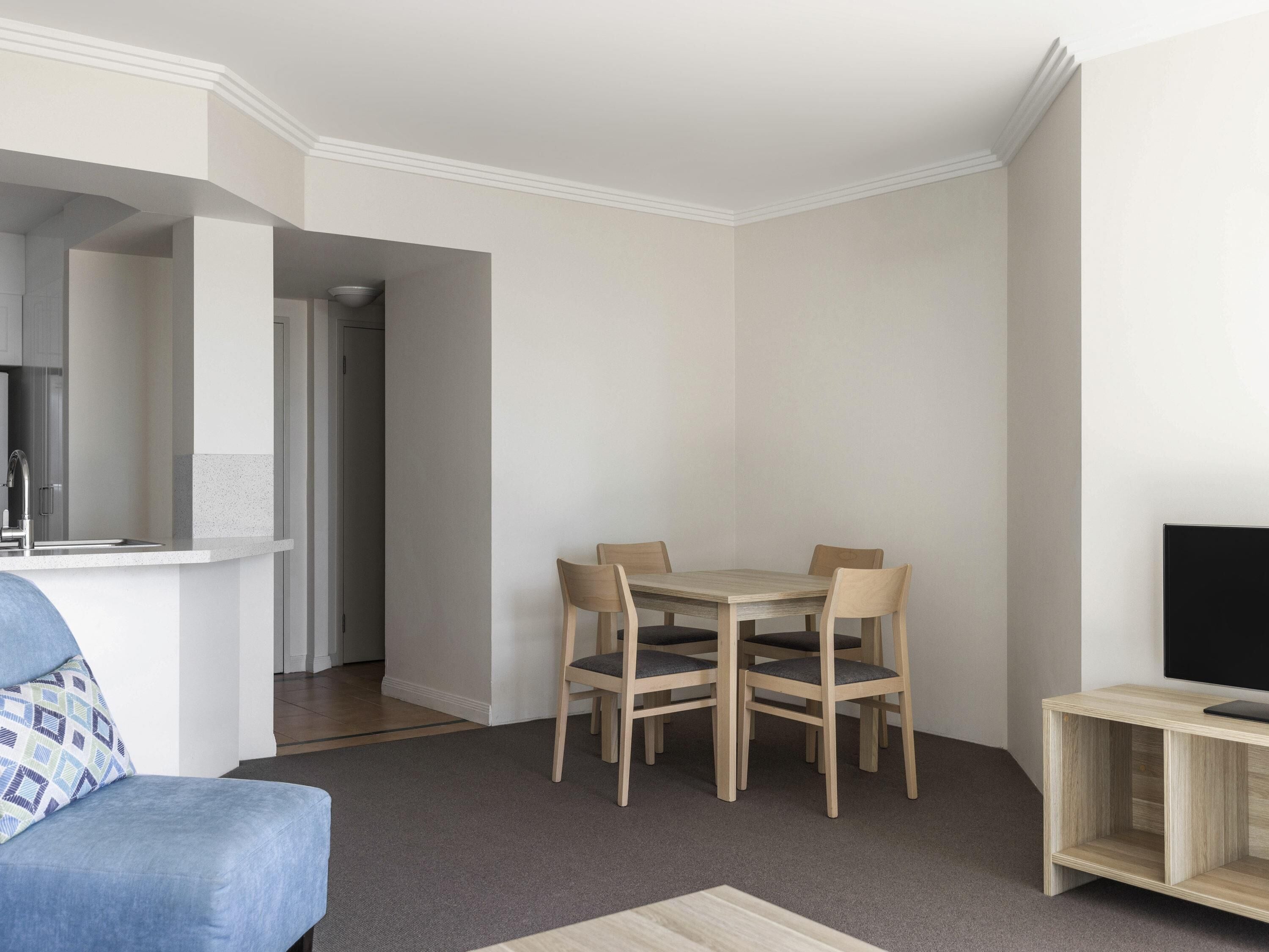 Una sala moderna con comedor, un sofá, un televisor sobre un mueble bajo y una cocina al fondo.