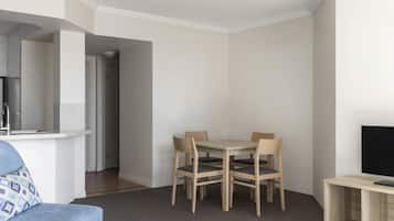 Una sala moderna con comedor, un sofá, un televisor sobre un mueble bajo y una cocina al fondo.