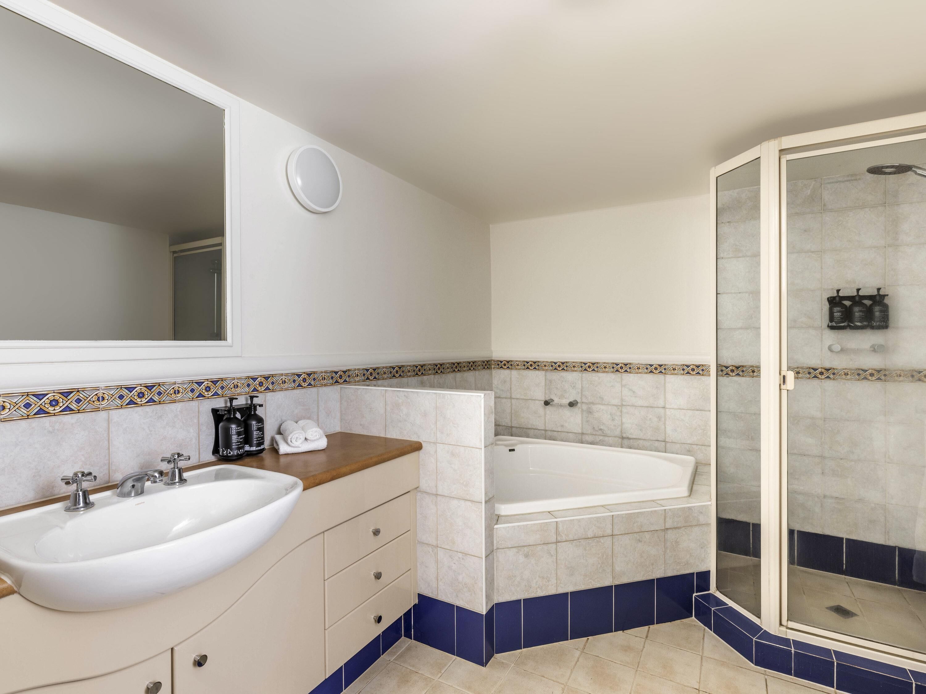 Un baño con lavamanos, espejo, tocador y zona de ducha.