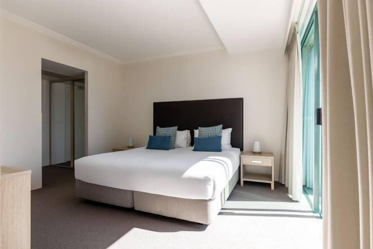 Una camera d'albergo con un letto grande, un comodino e una finestra con tende.