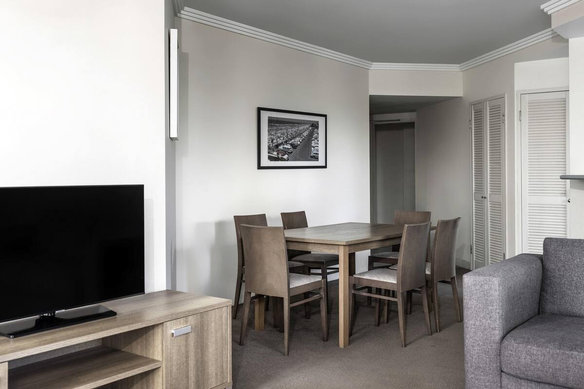 A modern living room with a flat-screen TV, a wooden dining table, and six chairs.