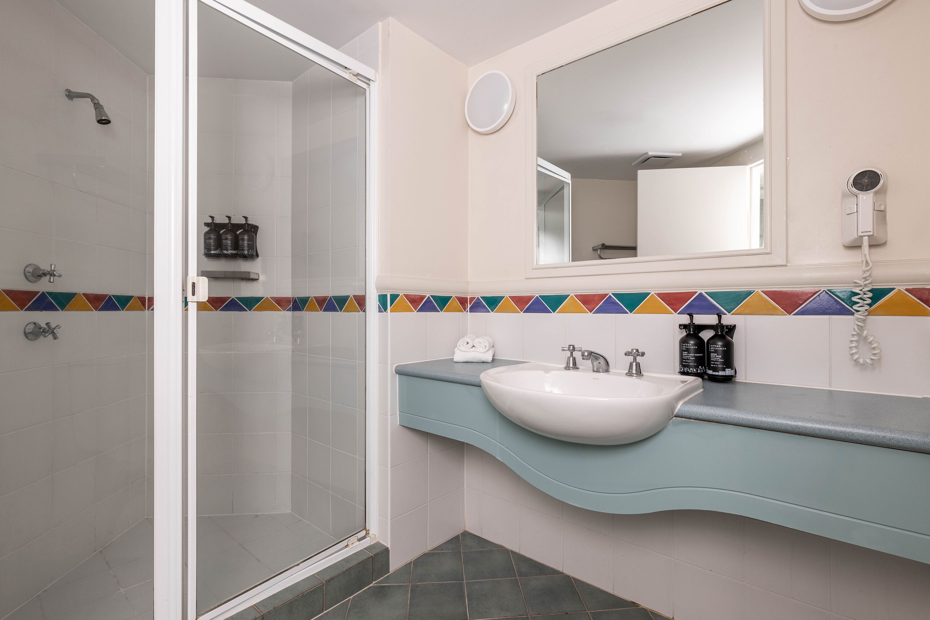A bathroom with a shower, a sink, a mirror, and a towel rack.