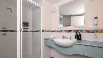 A bathroom with a shower, a sink, a mirror, and a towel rack.
