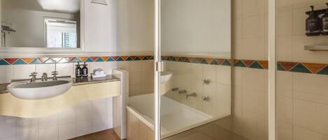 A bathroom with a sink, mirror, shower, and tiled walls.
