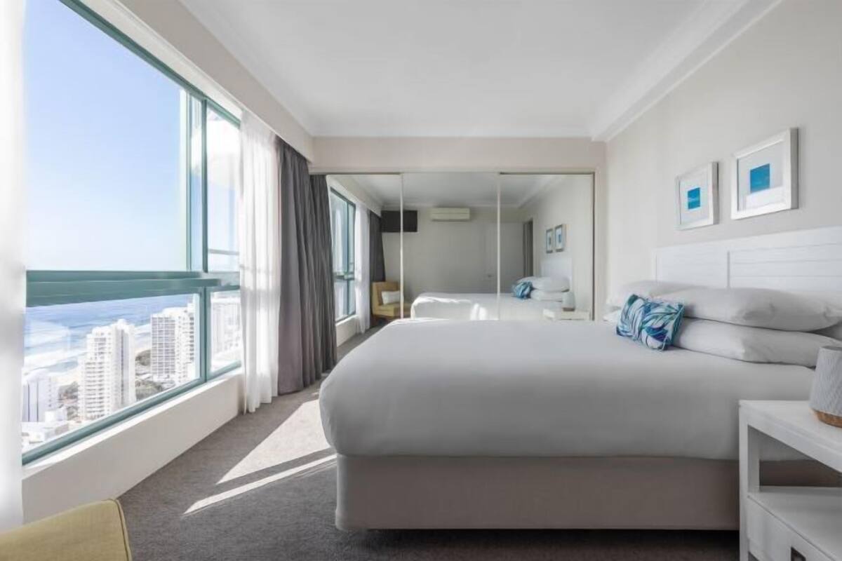 Camera d'albergo con un letto grande, un comodino, una scrivania e una finestra che si affaccia su edifici, oltre a uno specchio.