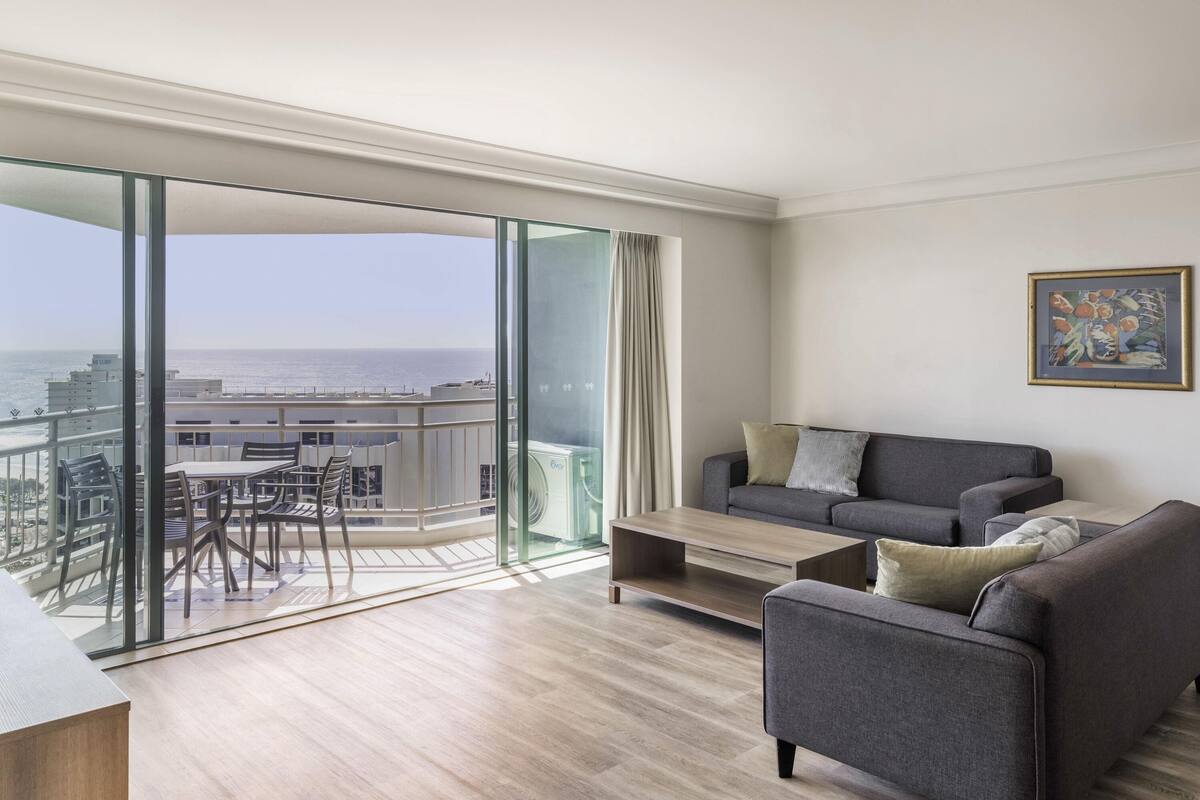 A modern living room with a grey sofa, a coffee table, and a view of the city and ocean.