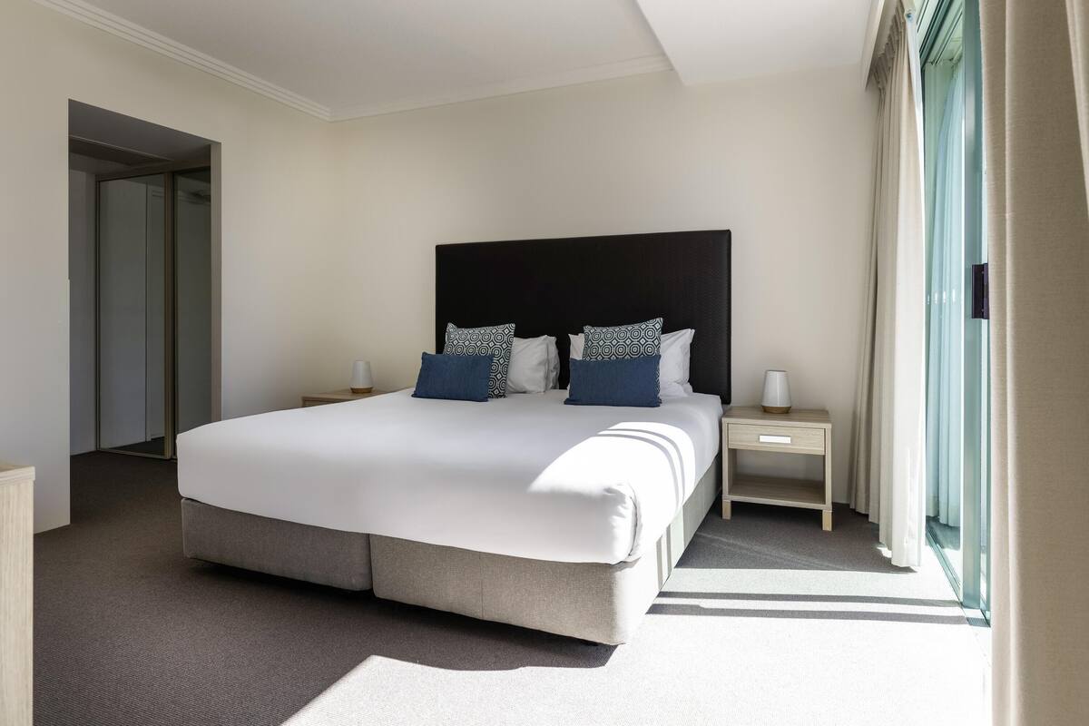 A hotel room with a large bed, bedside tables, a mirror, and a view of the outdoors.