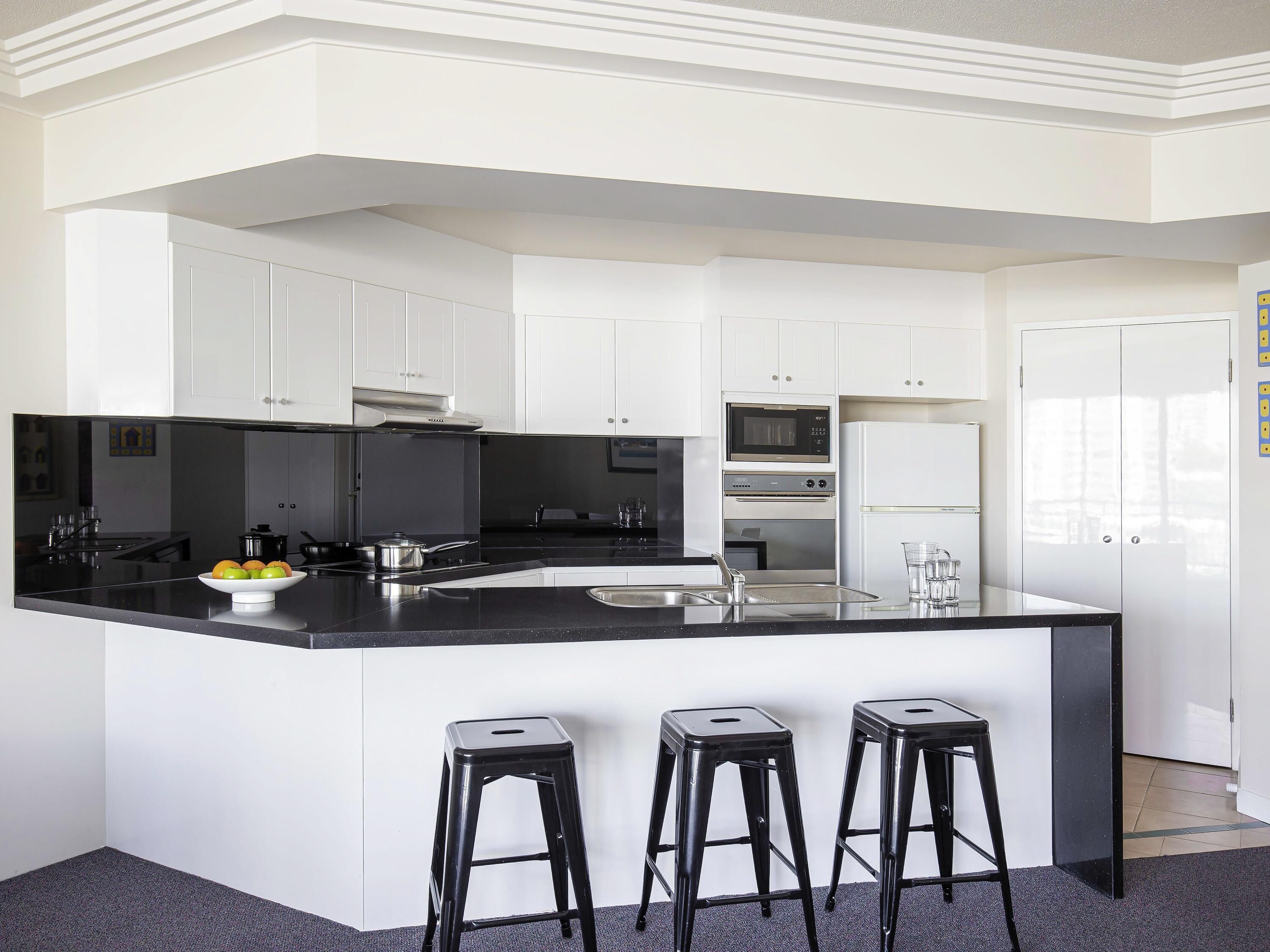 Una cocina moderna con armarios blancos, encimera negra, horno empotrado y refrigerador.