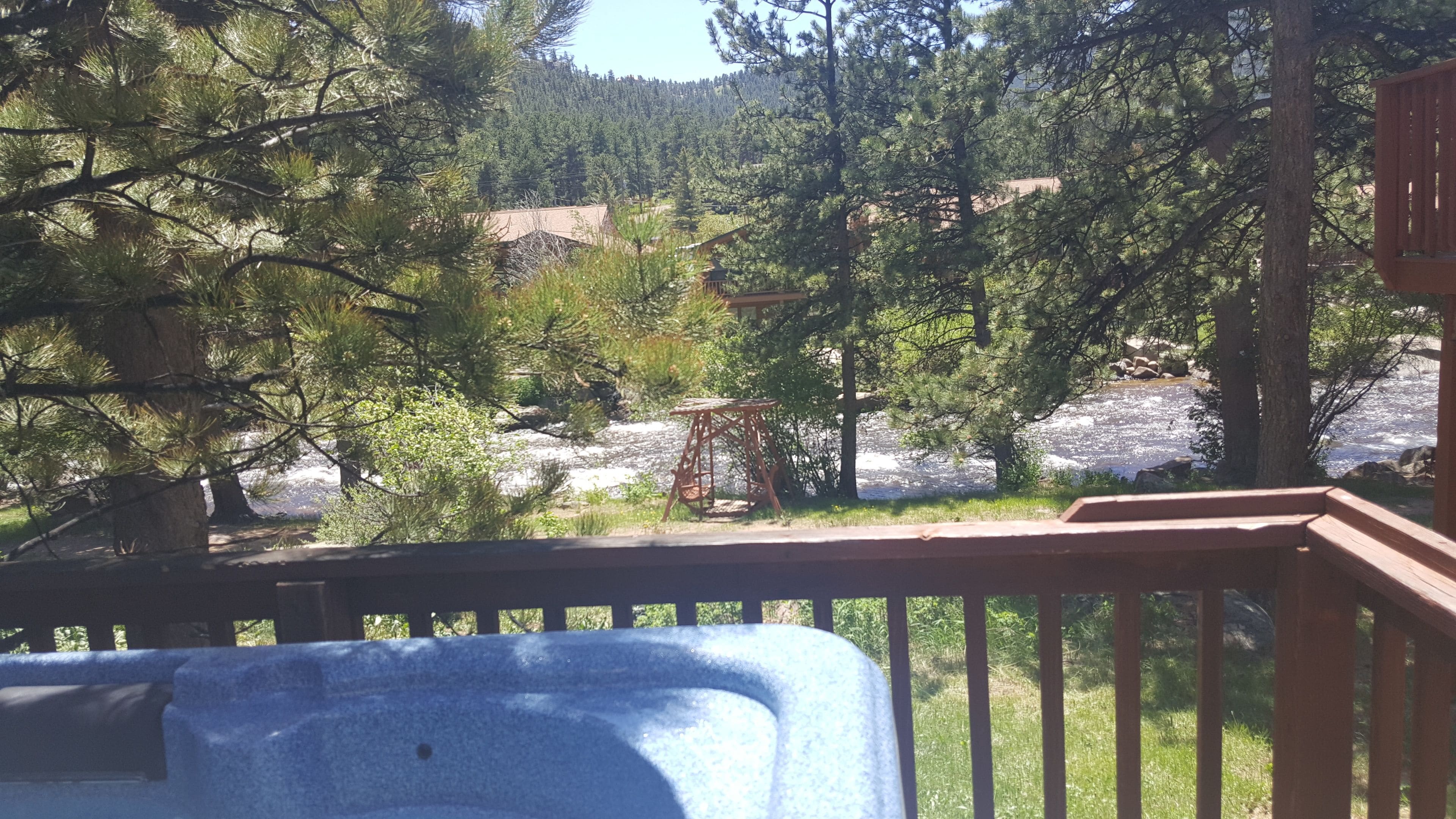 Une terrasse en bois donnant sur une rivière, avec des arbres et une chaîne de montagnes en arrière-plan.