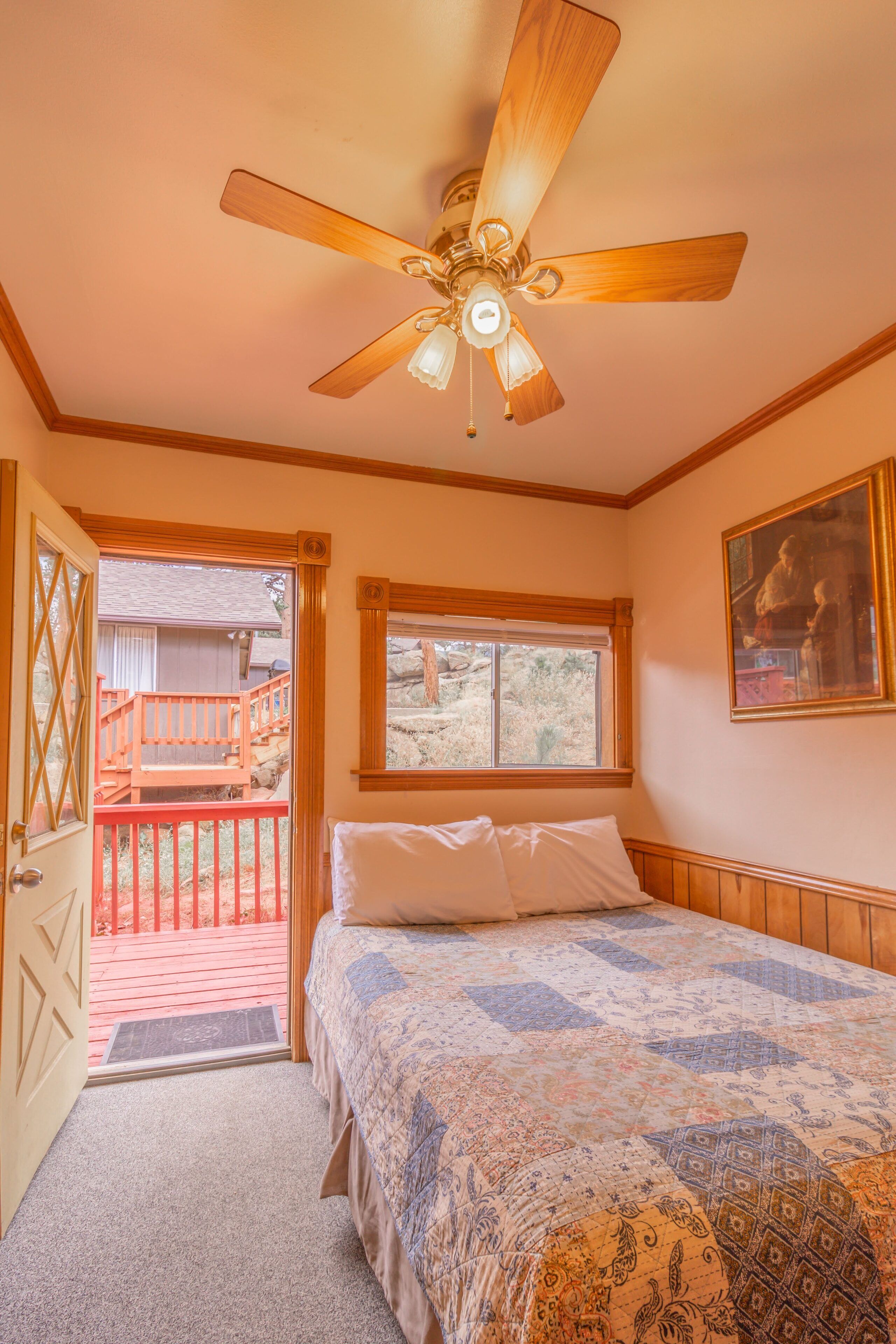 A bedroom with a bed, a ceiling fan, a window, and a door leading to an outdoor deck.