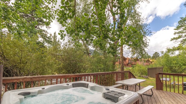 Un jacuzzi en una terraza de madera con una mesa de picnic y un cobertizo pequeño al fondo.