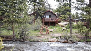 Una cabaña con terraza que da a un río, rodeada de árboles.