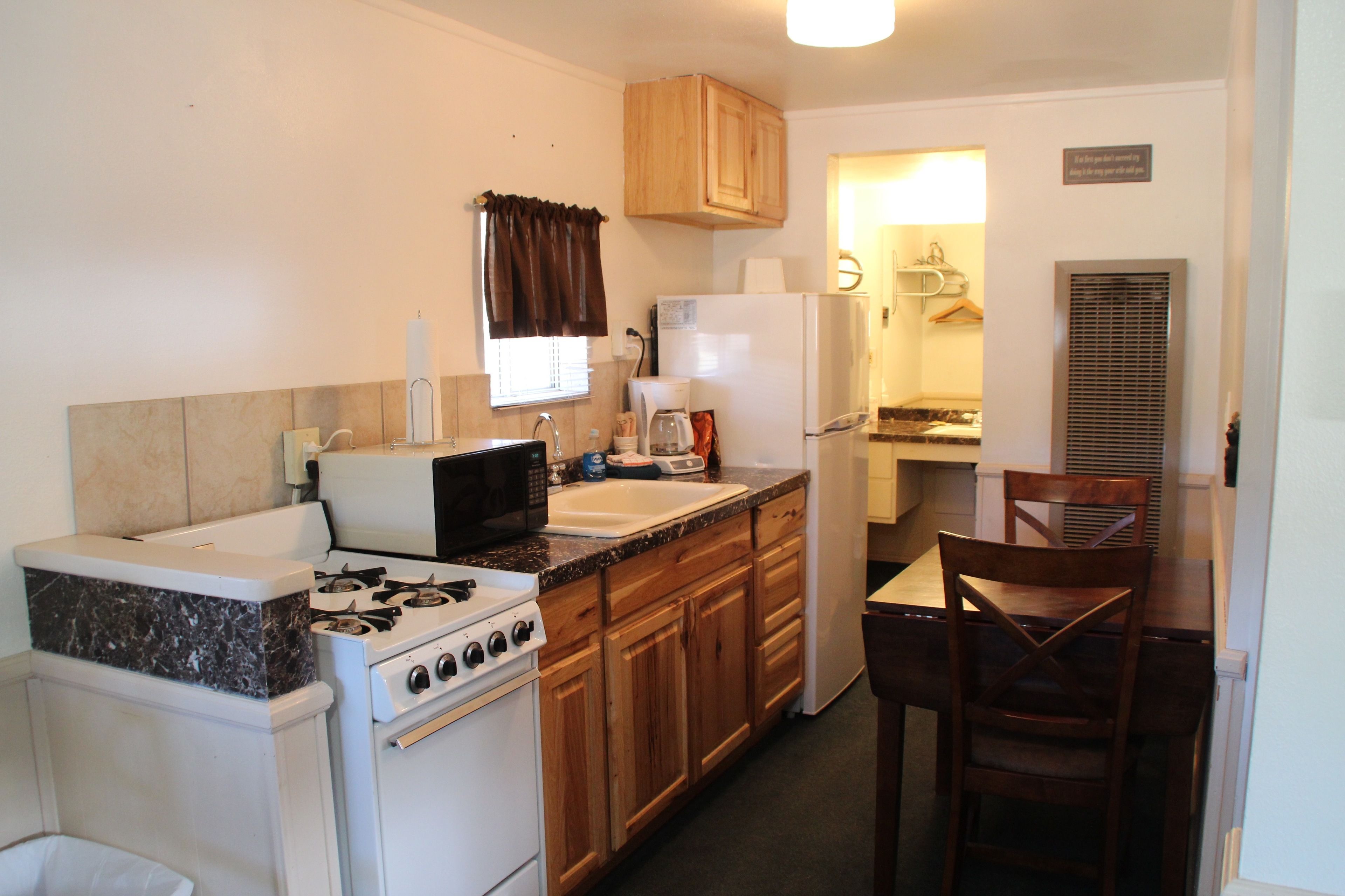 A compact kitchen with a stove, sink, and refrigerator. There is a dining area with a table and chairs.