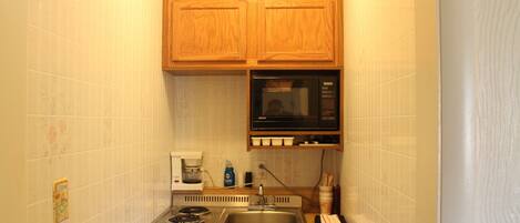 A compact kitchen with wooden cabinets, a microwave, a stove, and a coffee maker.