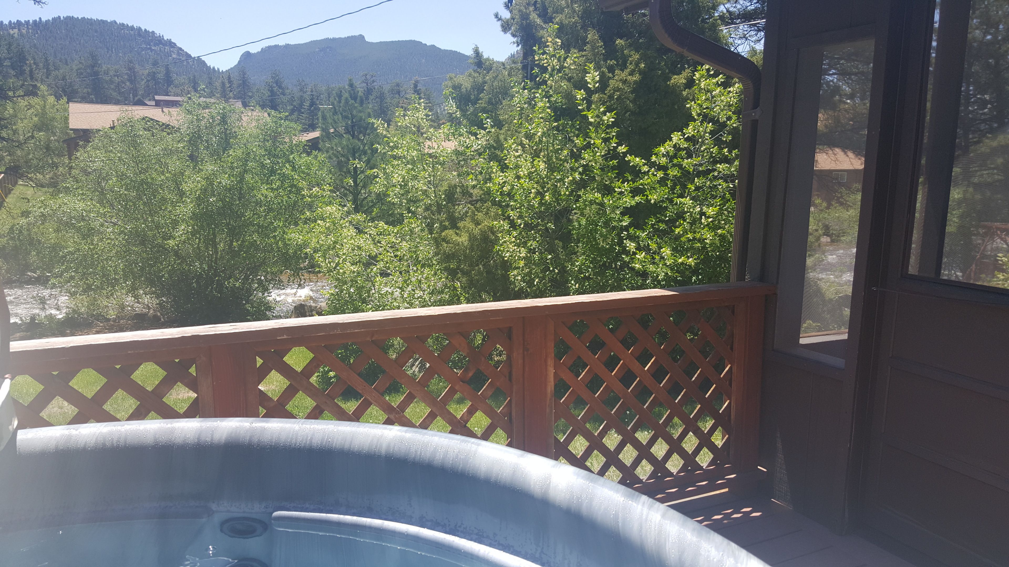 Un bain à remous sur une terrasse en bois, avec vue sur une forêt et des montagnes en arrière-plan.