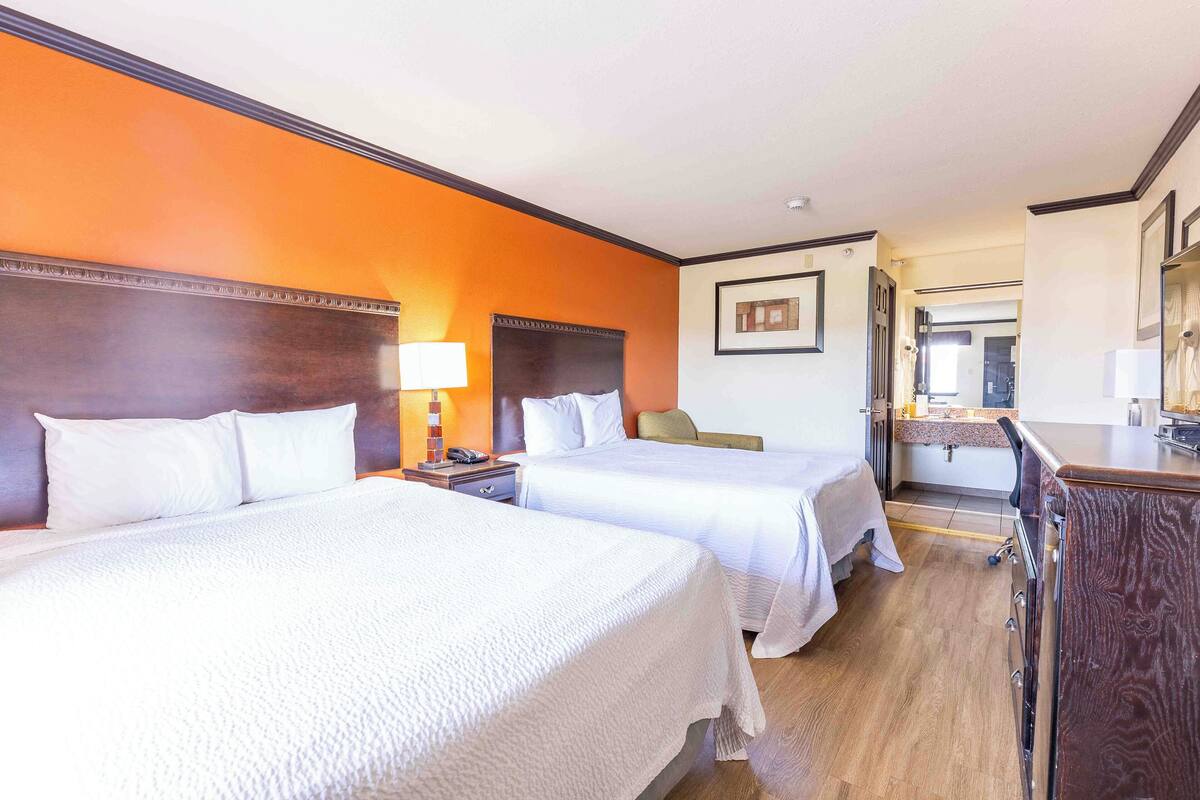 Habitación de hotel con dos camas, una mesita de noche, una lámpara, una silla y un aparador de madera.