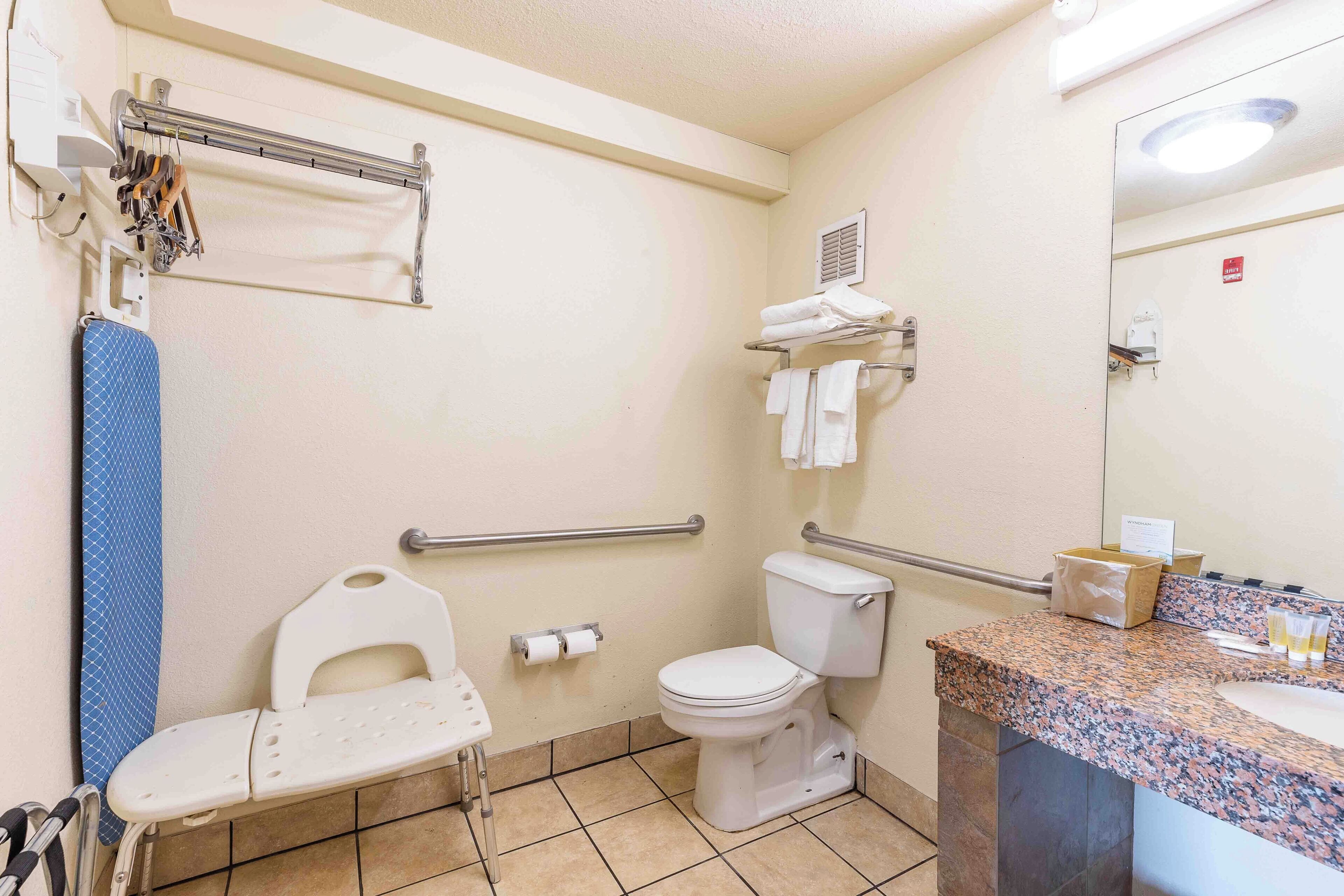 A bathroom with a white toilet, a sink with a granite countertop, a mirror, a towel rack, and a grab bar.
