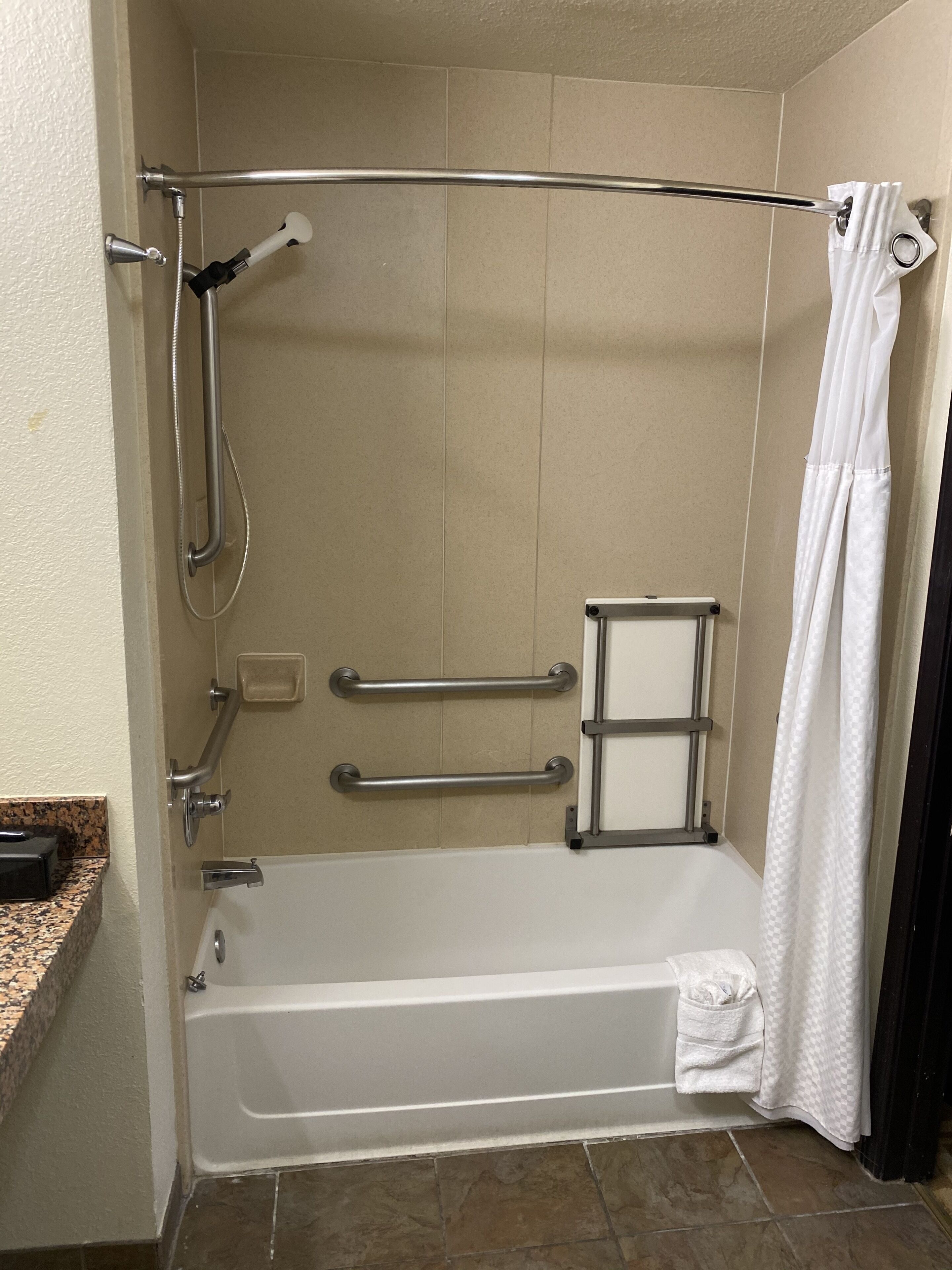 A standard shower stall with a grab bar, a handheld showerhead, and a white shower curtain.