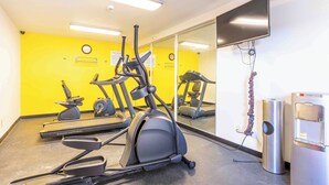 Une salle de sport équipée de matériel d’exercice, d’un miroir et d’un réfrigérateur.