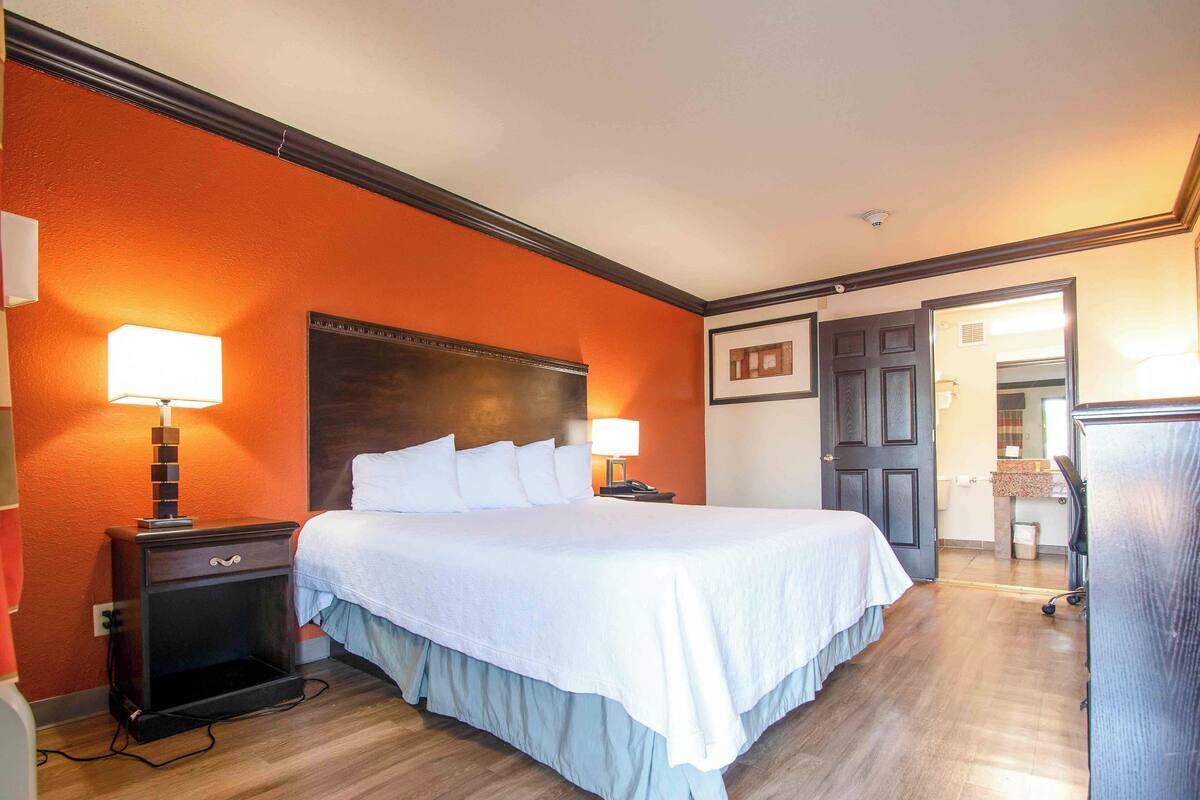 Habitación de hotel con una cama grande, dos mesitas de noche con lámparas, un cabecero de madera y una puerta que da a otra habitación.