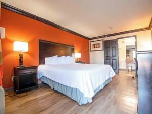 A hotel room with a large bed, two bedside tables with lamps, a wooden headboard, and a door leading to another room.