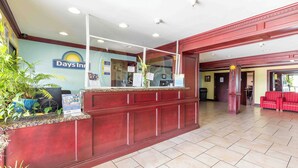 Un espace d’accueil comprenant un comptoir de réception, une grande enseigne Days Inn et un coin salon avec des chaises rouges.