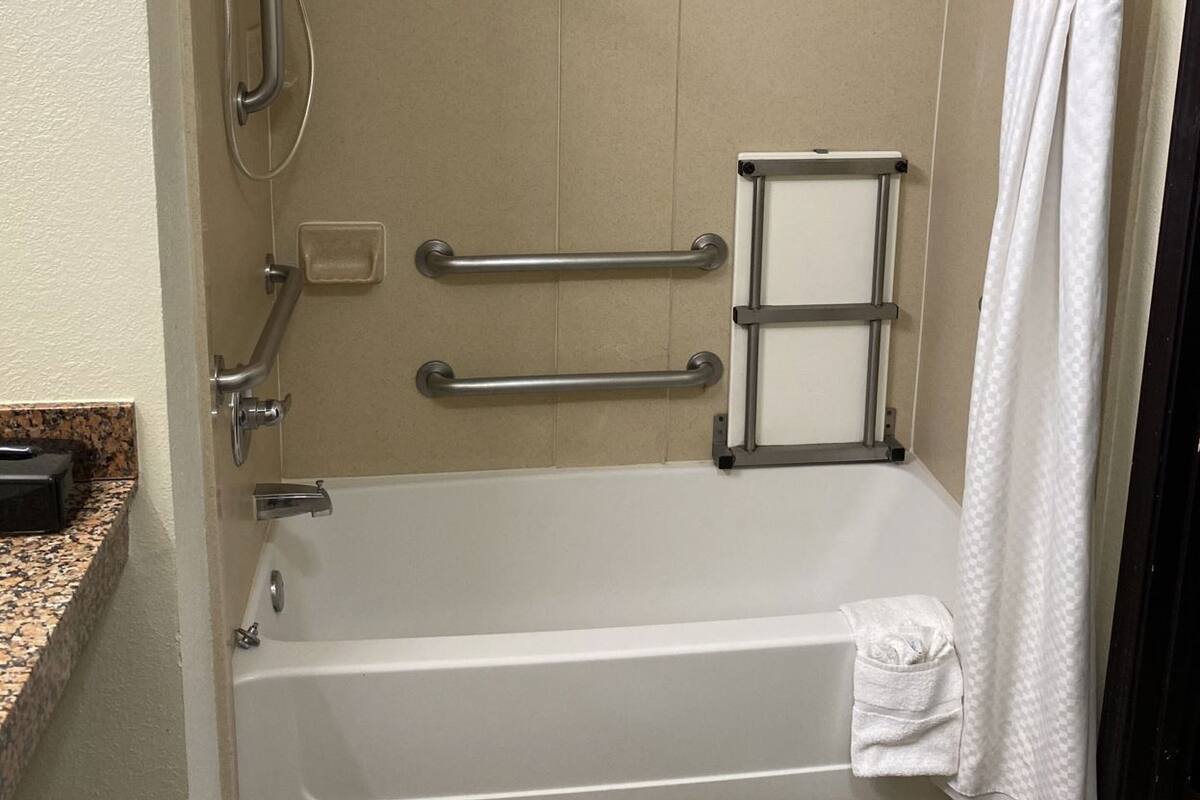 Un baño con bañera, barras de apoyo, cortina de ducha y un perchero.
