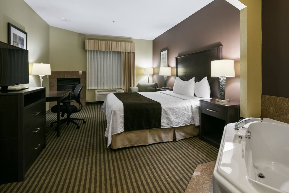 Une chambre d’hôtel équipée d’un lit, d’un bureau, d’une chaise, de lampes et d’une baignoire.