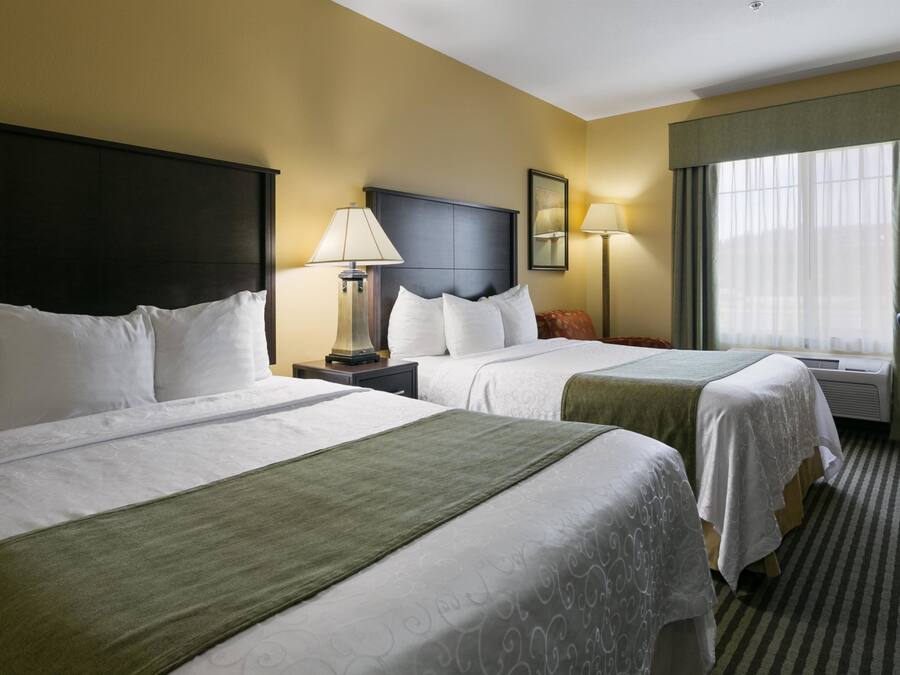 A hotel room with two beds, a desk, a chair, a lamp, and a window with curtains.