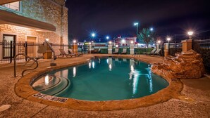 Un espace piscine aménagé pour la nuit, avec un jacuzzi, des chaises longues et, au fond, un panneau indiquant qu'on y loue des camions U-Haul.