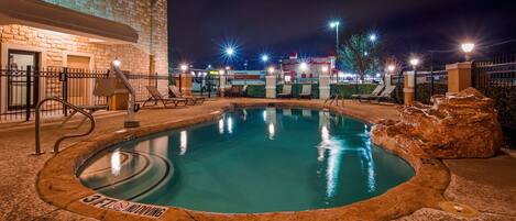 A nighttime pool area with a hot tub, lounge chairs, and a U-Haul rental sign in the background.