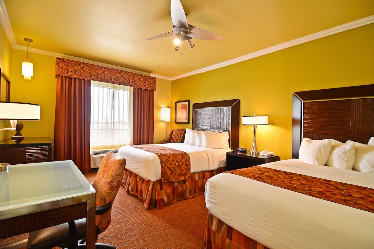 Quarto de hotel com duas camas, uma escrivaninha e um ventilador de teto.