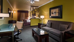 Une chambre d’hôtel comprenant un lit, un canapé, un bureau avec une chaise, une lampe sur pied et un tableau au mur.