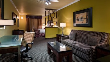A hotel room with a bed, a sofa, a desk with a chair, a standing lamp, and a painting on the wall.