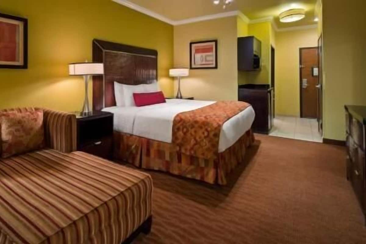 Quarto de hotel com cama, duas mesas de cabeceira com abajures, um sofá e piso coberto por carpete.
