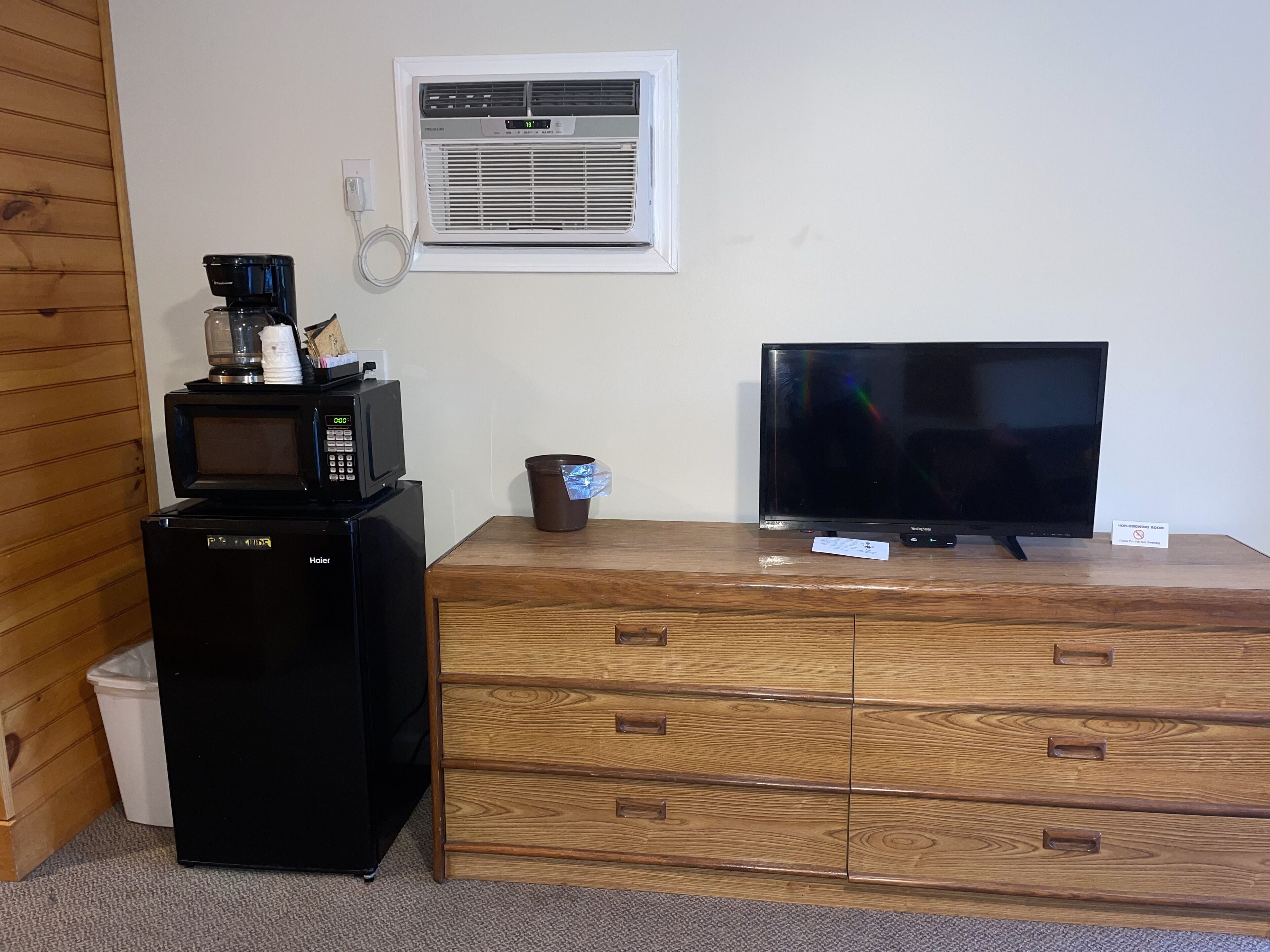 A compact kitchenette with a microwave, coffee maker, and a small trash bin. A flat-screen TV is placed on a wooden dresser.