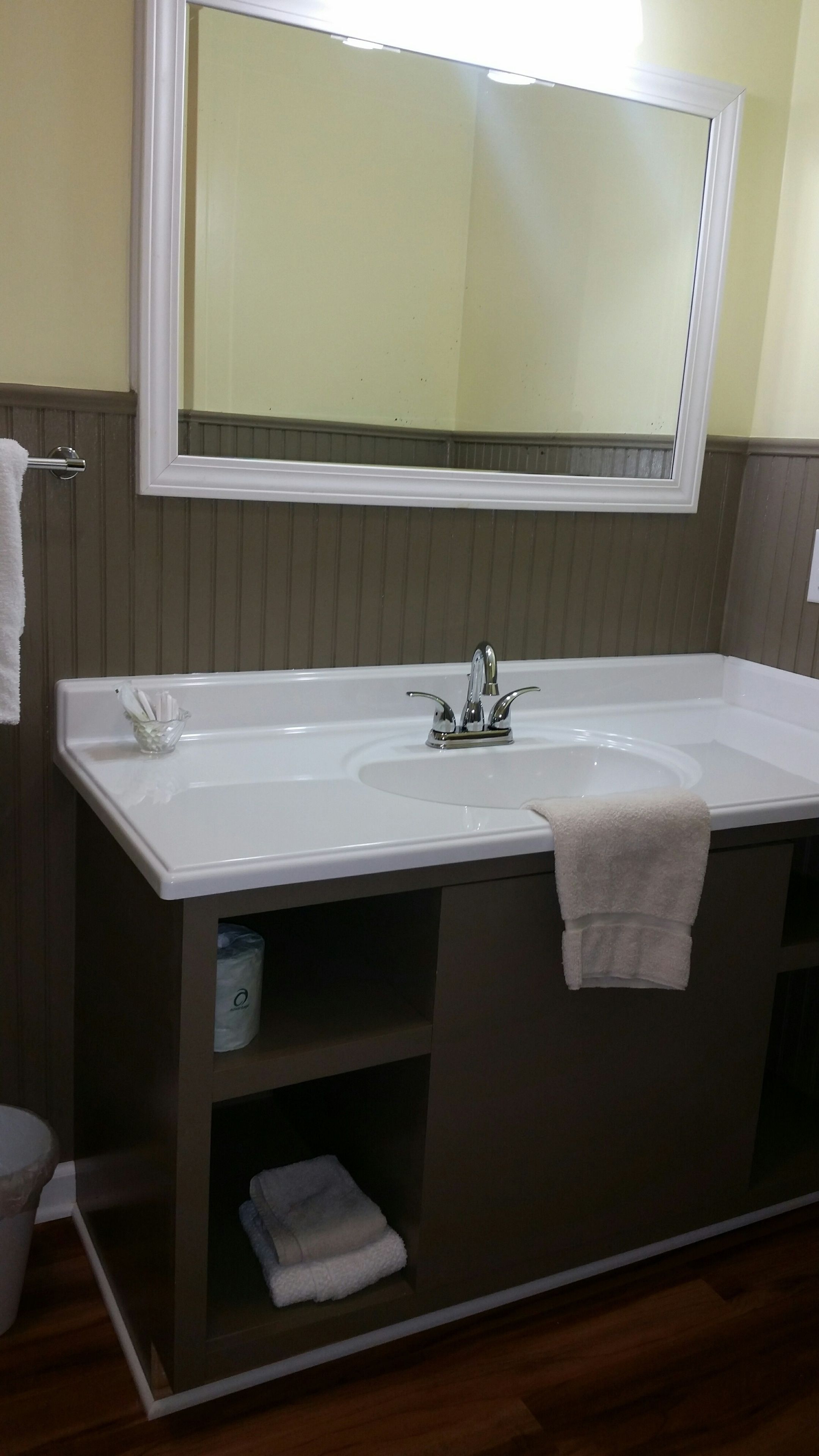 Un bagno con un lavandino grande e bianco, uno specchio sopra e un porta asciugamani. Sul piano del lavandino c'è un piccolo contenitore di vetro.