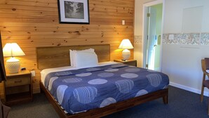 A bedroom with a wooden headboard, a bed with a blue patterned bedspread, two bedside lamps, and a framed picture on the wall. - A Holiday Motel (Maggie Valley)