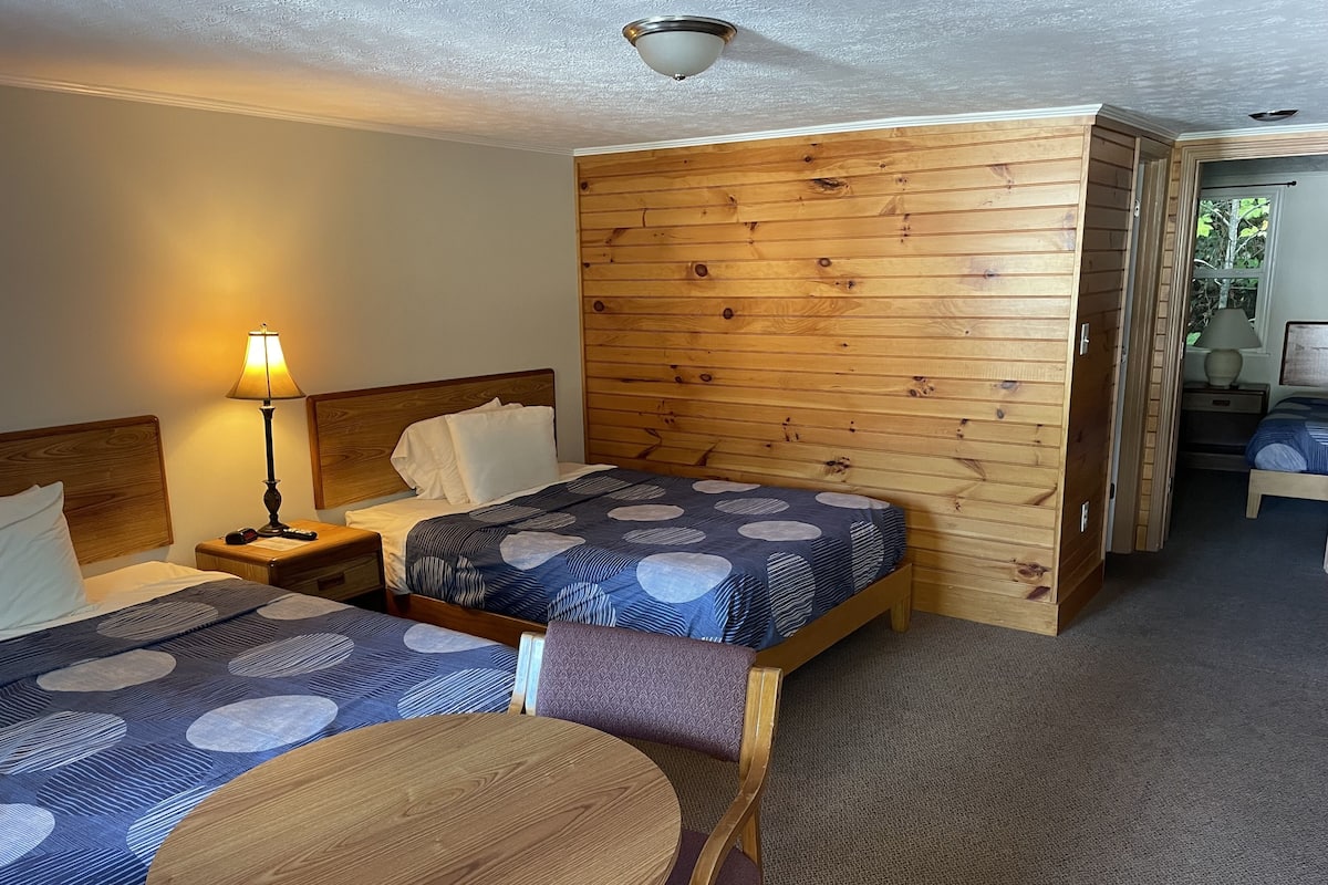 A hotel room with two beds, a round wooden table, and a wooden partition wall.