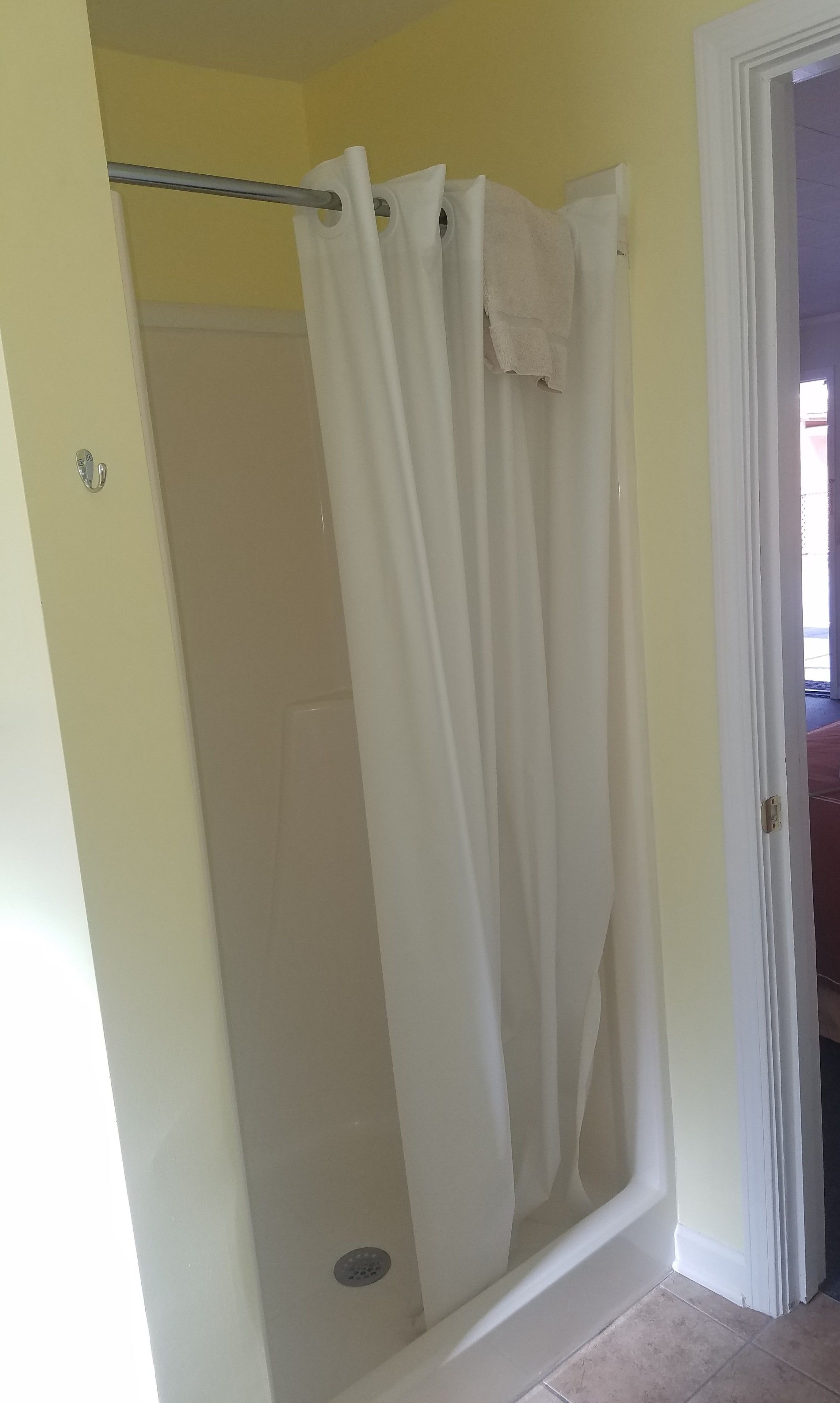 A shower area with a white curtain, a visible showerhead, and a door leading to another room.
