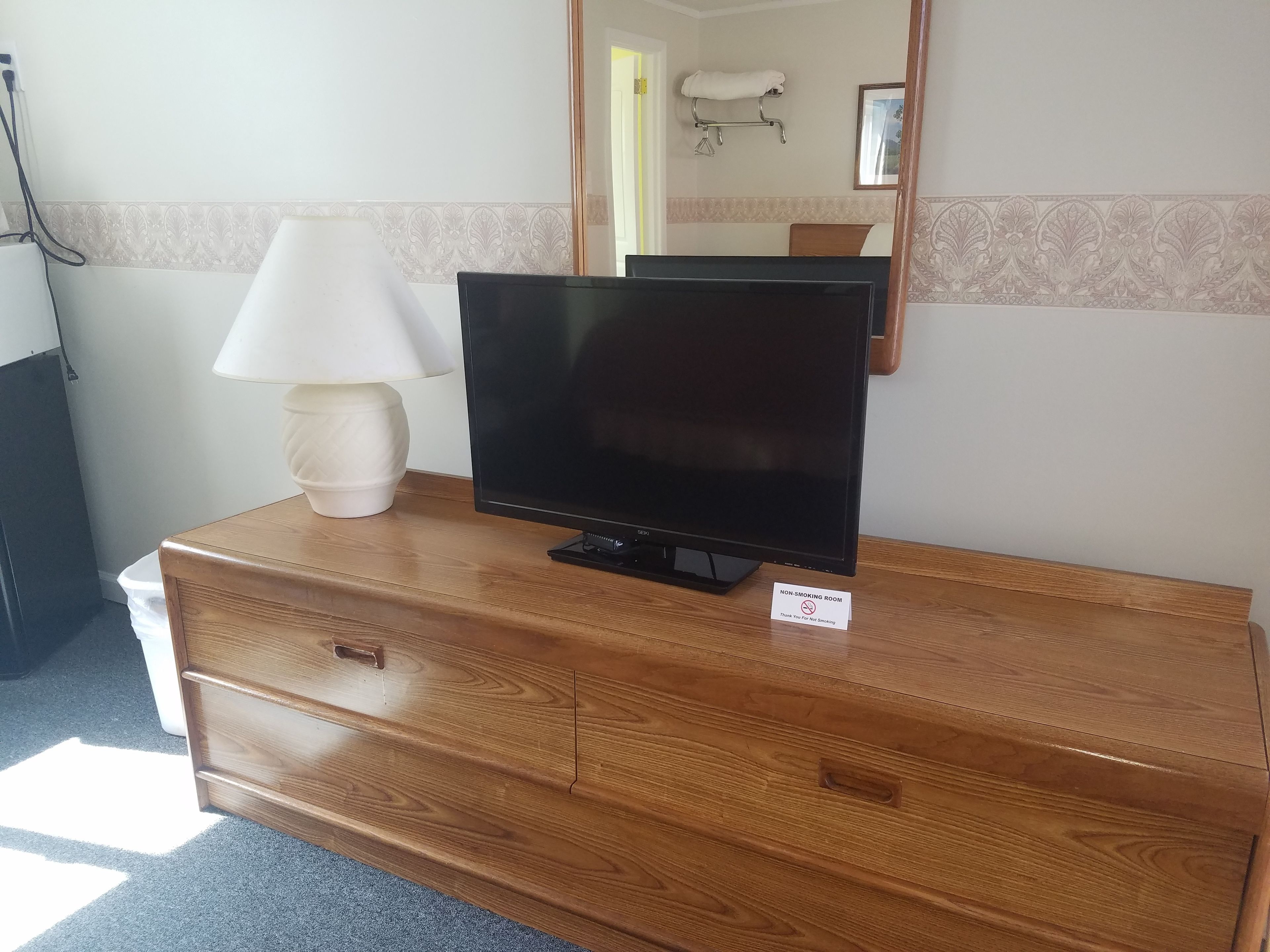 Un comò in legno con una televisione a schermo piatto, una lampada bianca e il cartello ‘non fumatori’.