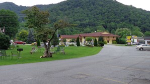 A motel with a parking lot, outdoor seating, and a mountain backdrop. - A Holiday Motel (Maggie Valley)