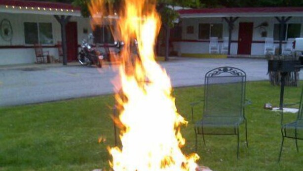 A stone fire pit with a roaring fire in the center, surrounded by a grassy area. - A Holiday Motel (Maggie Valley)